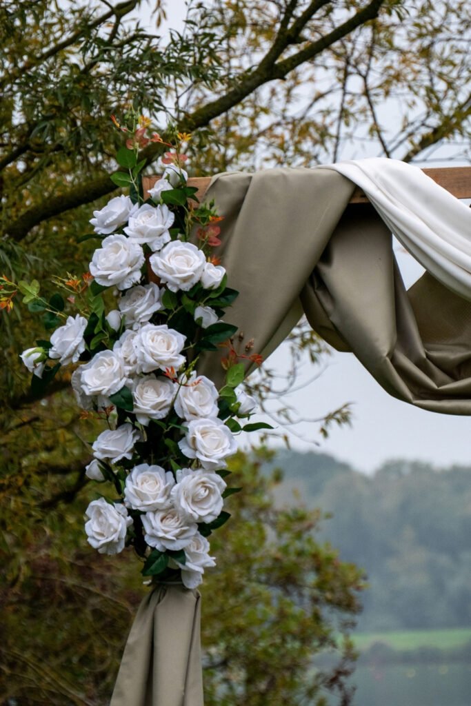 Outdoor wedding arch with white roses and soft draped fabric