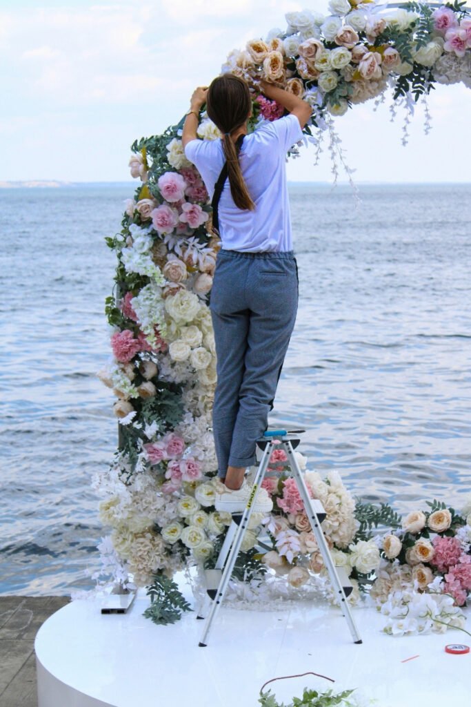 Decorating a flower arch from a ladder at a seaside ceremony