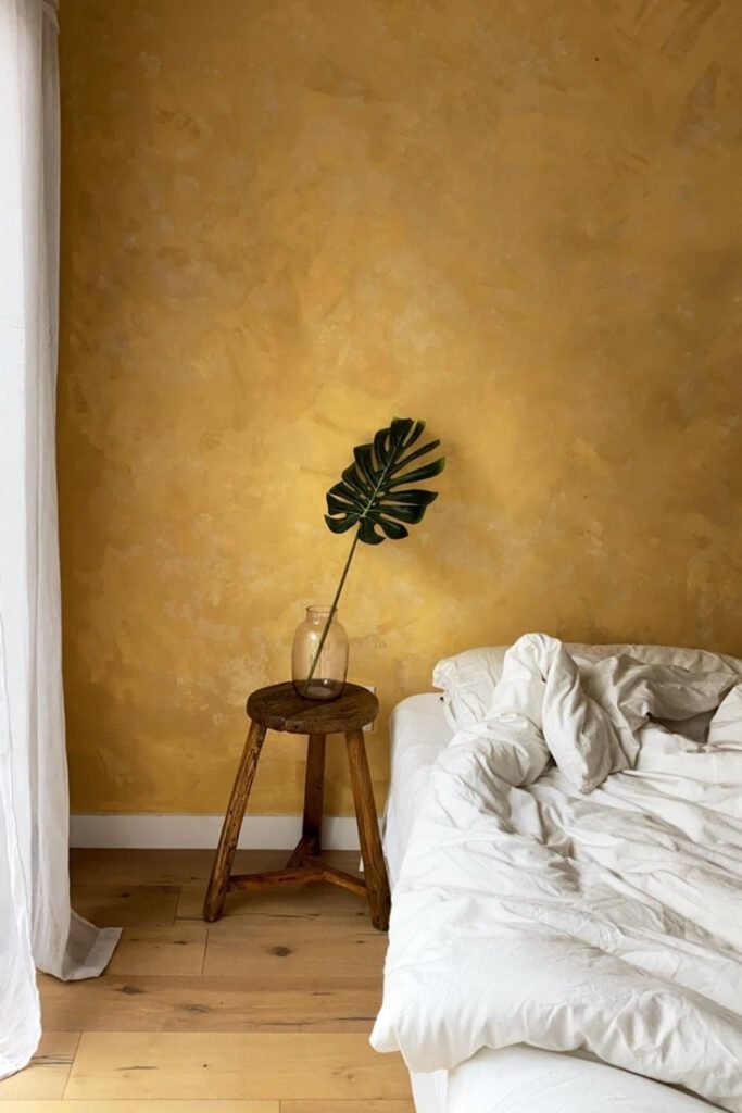 Bedroom with a warm ochre limewash wall and a tropical leaf in a vase