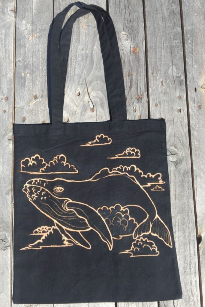 Black canvas tote bag with a bleach-painted whale and clouds