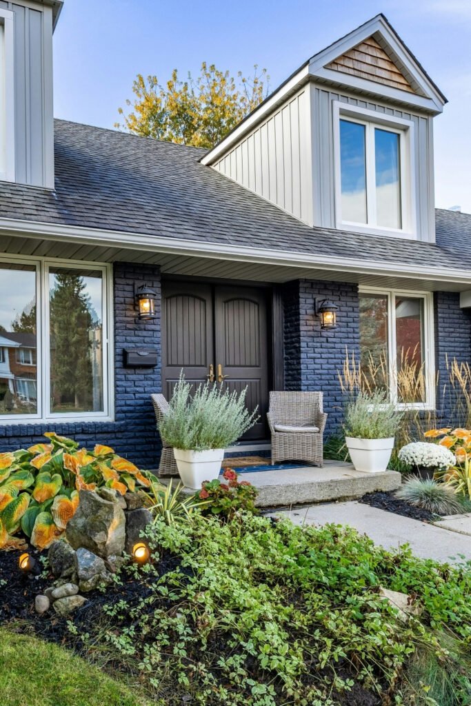 Small front yard flower bed in front of a house with blue brick siding