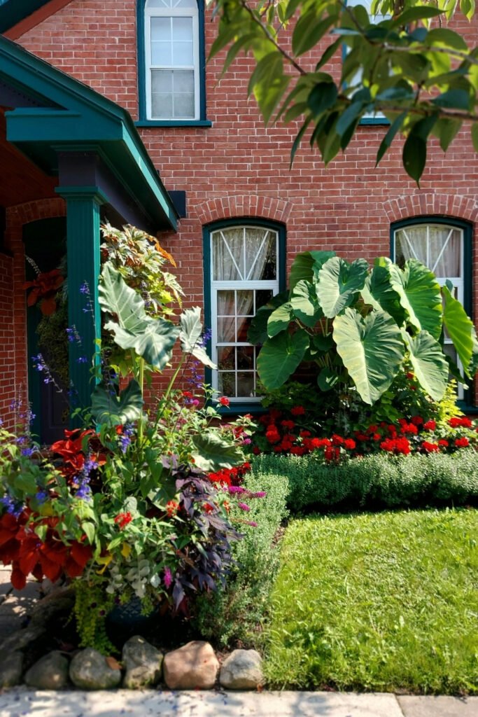 Red and white flowers planted in layers in front of a brick house