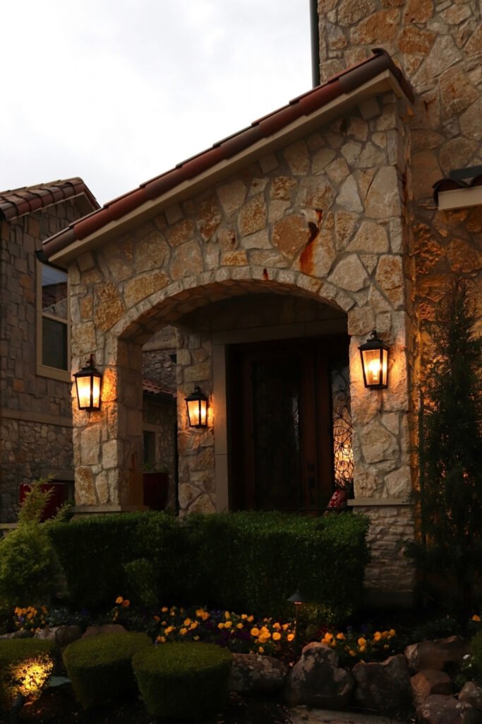 Classic wall lanterns lighting a stone house entrance surrounded by plants
