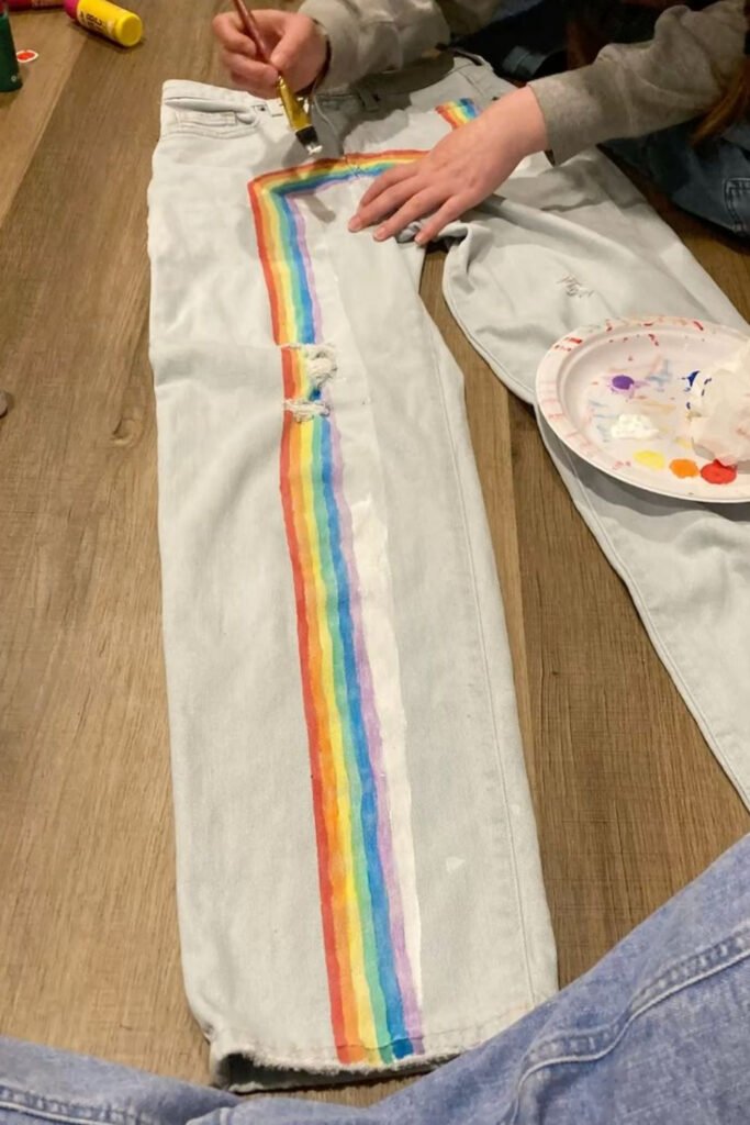 Painting rainbow stripes down the leg of white jeans