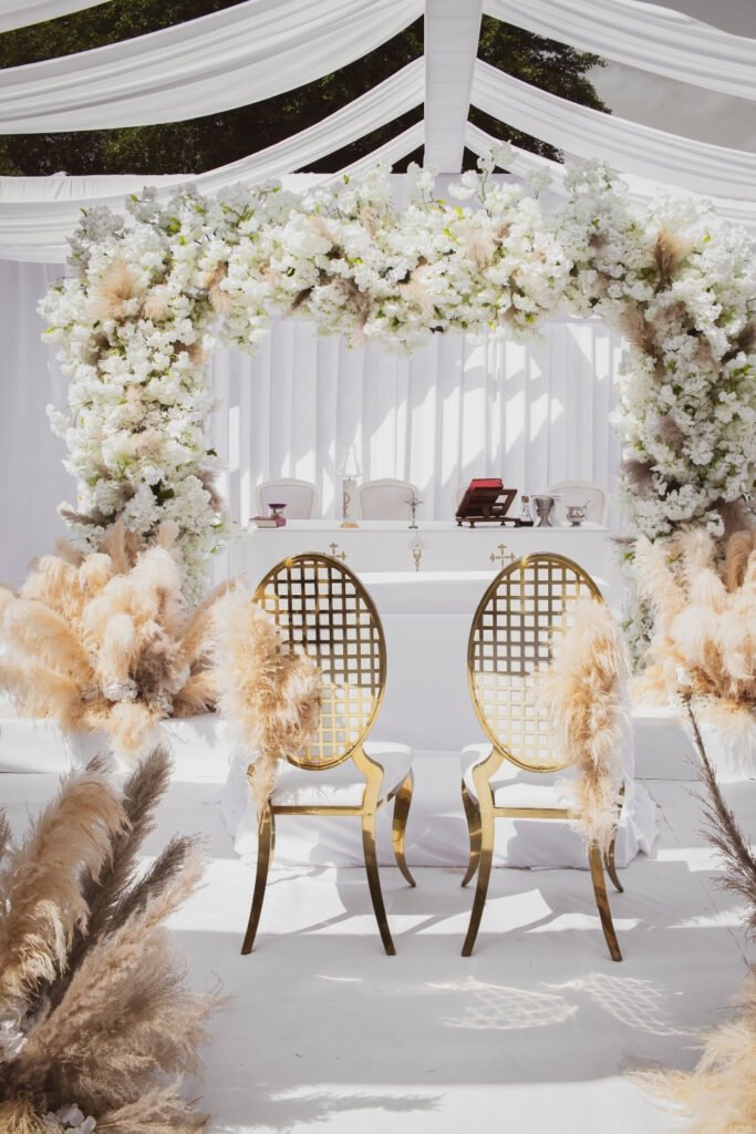 White floral canopy with gold chairs and pampas grass at a ceremony setup