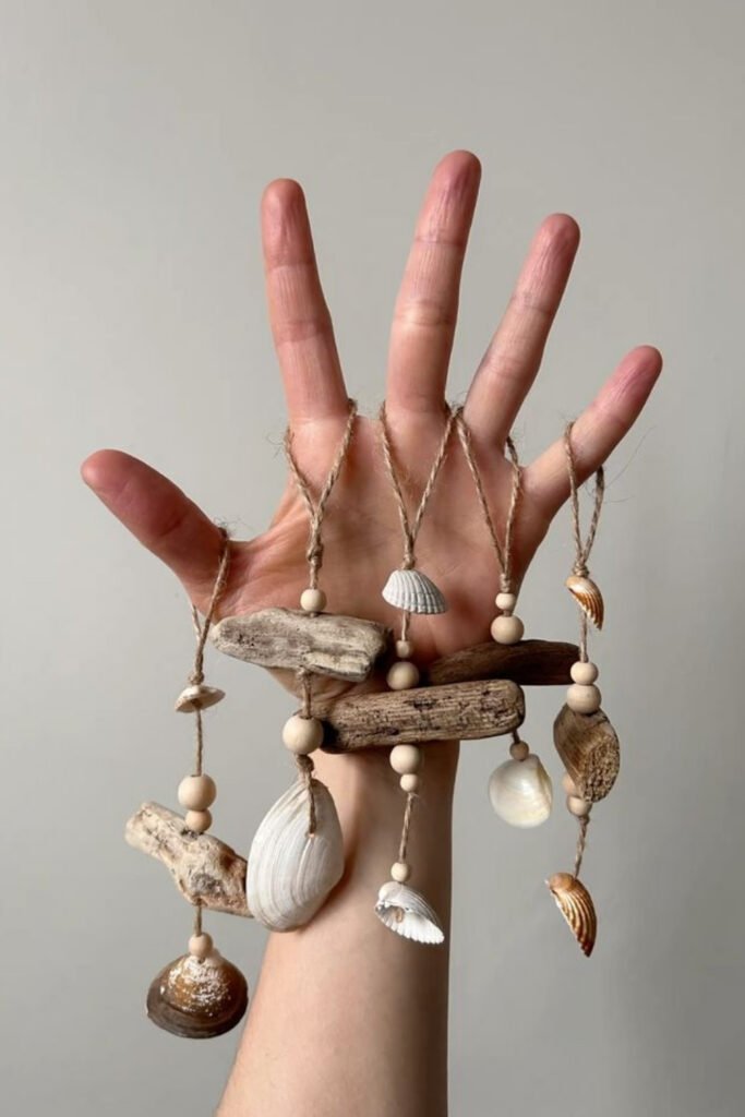 Hand holding a small homemade wind chime with shells, beads and driftwood
