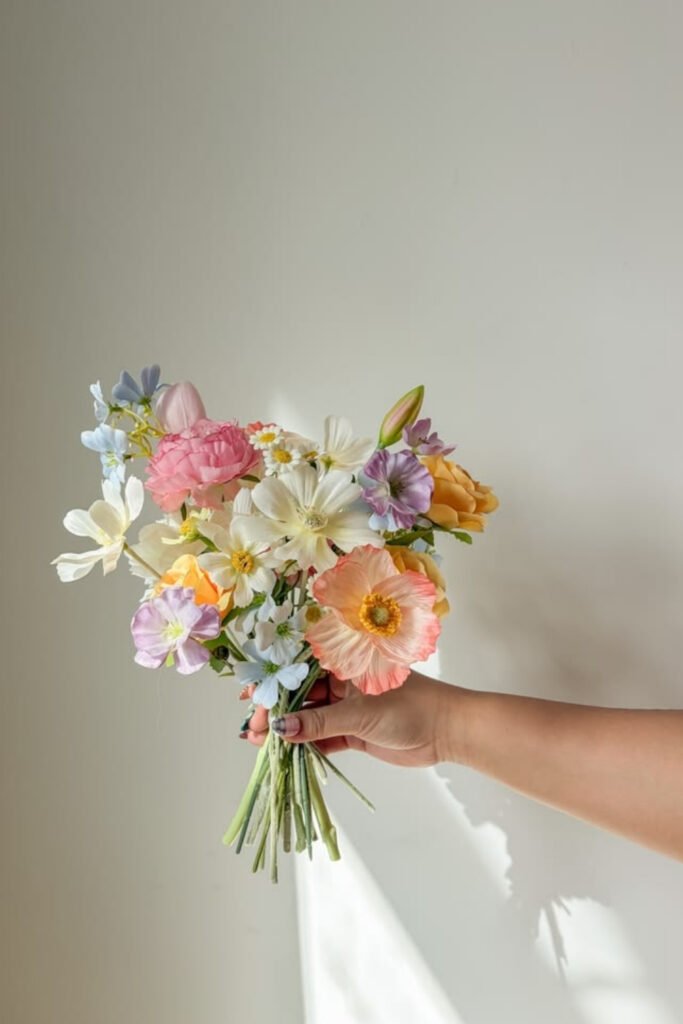 Small pastel bridal bouquet held against a plain wall