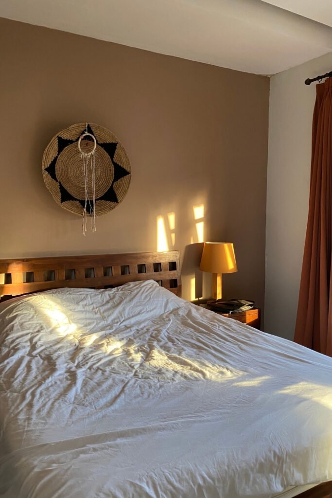 Sunlit bedroom with warm white walls, white bedding and a lamp