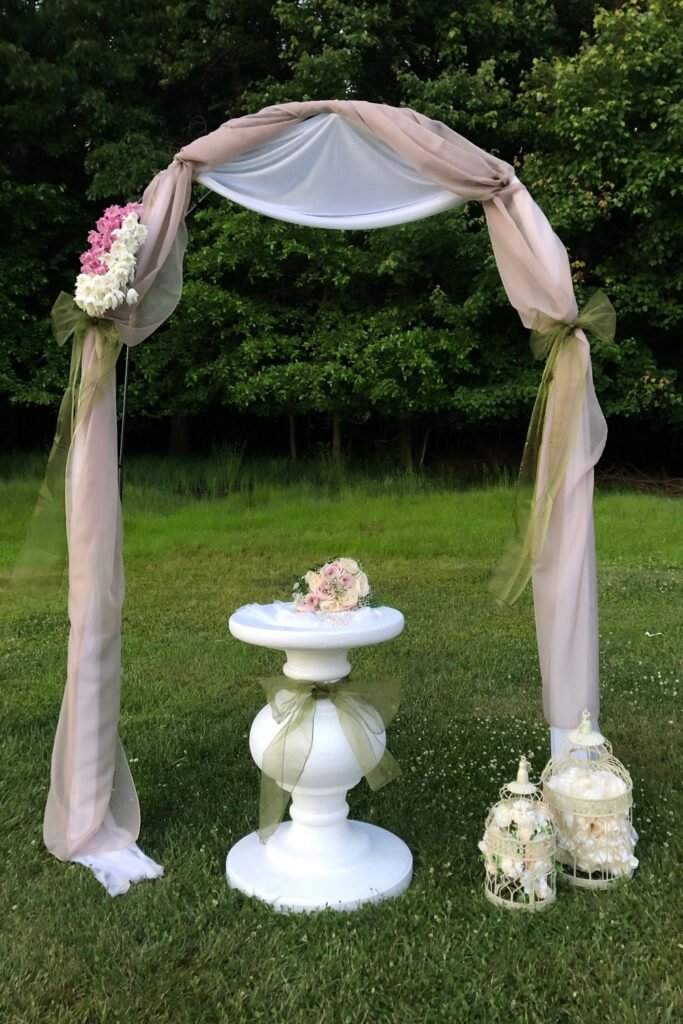 Simple arch draped in blush fabric with a small table on a meadow