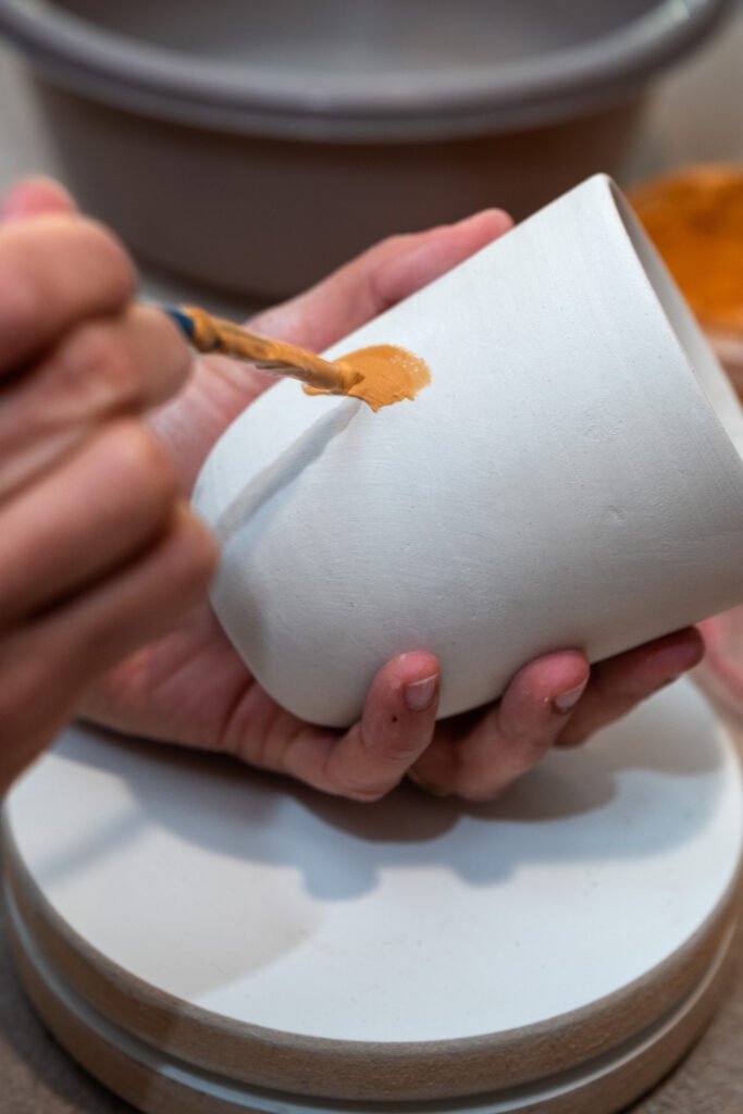 Hand painting a white ceramic cup with a thin brush