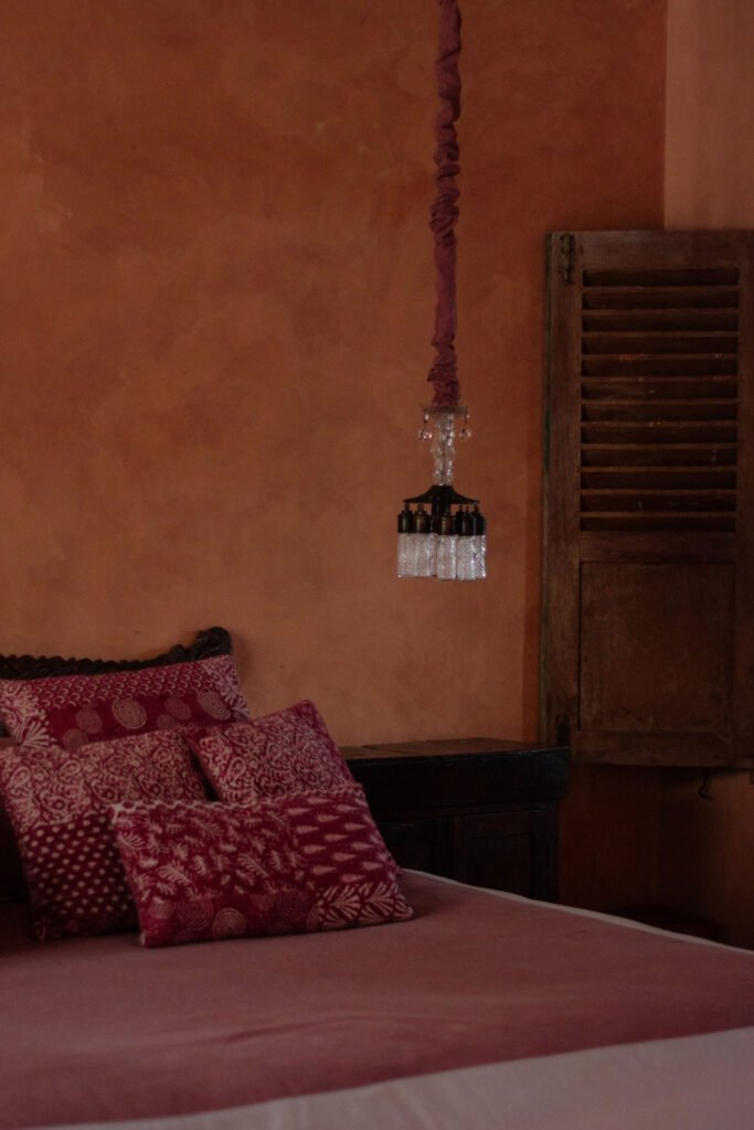 Rustic bedroom with terracotta red walls, red pillows and a hanging light