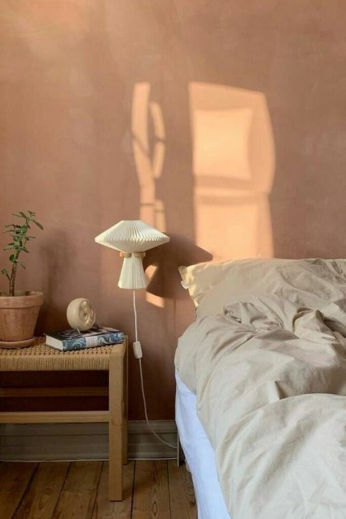Bedroom with a soft peachy pink wall, white bedding and a wooden side table