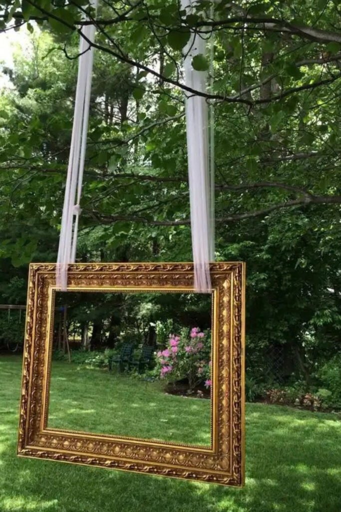 Ornate gold frame hanging from a tree in a garden as a photo backdrop