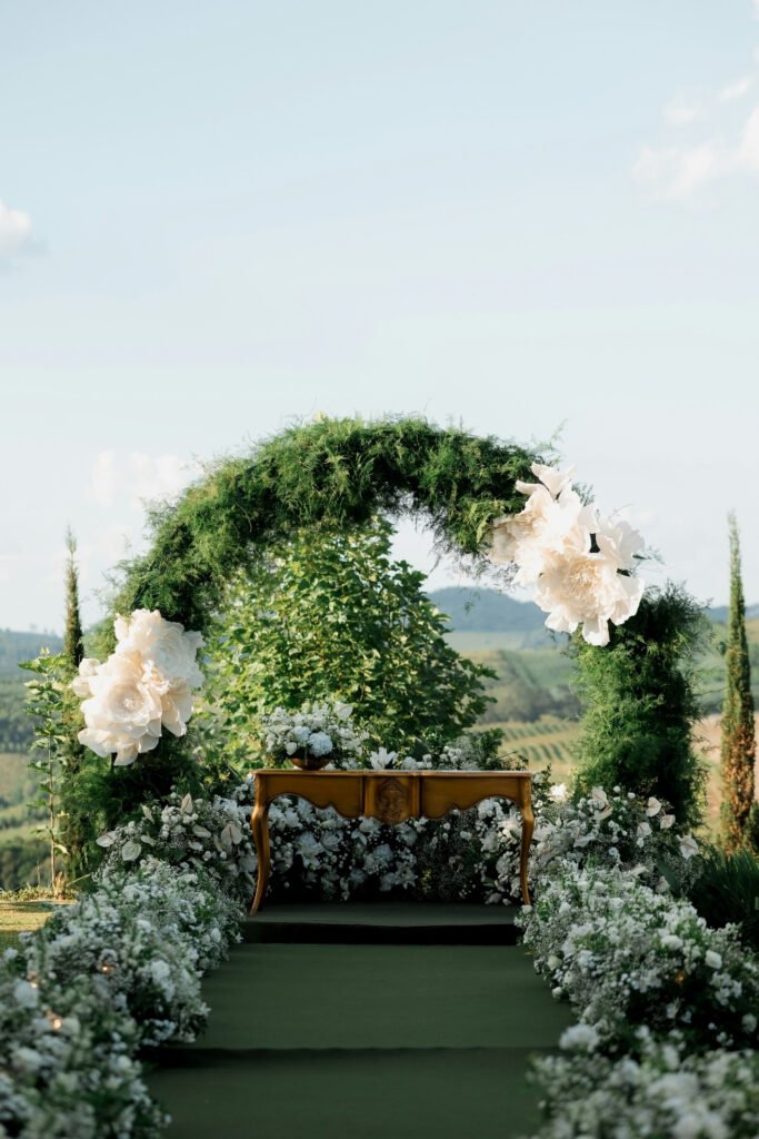 Green wedding arch with white flowers set against trees and open sky