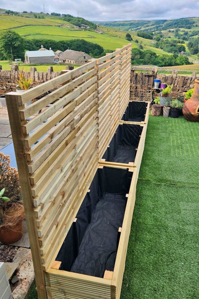 Long planter boxes with a wooden screen along a lawn
